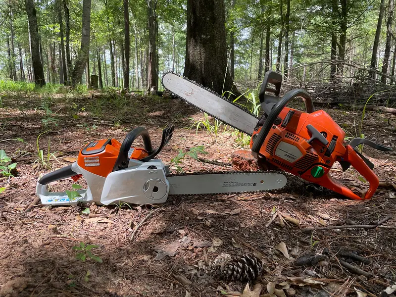 A battery chainsaw and a gas chainsaw resting side by side