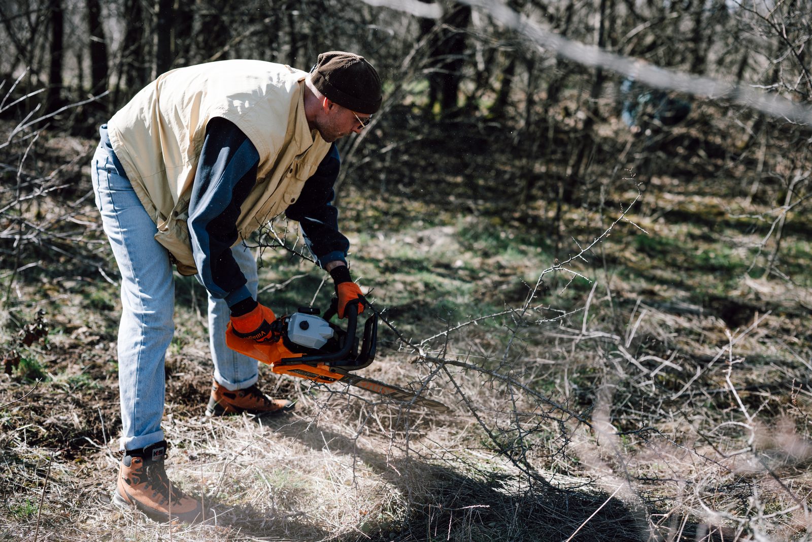 A person using a chainsaw to cut branches in a wooded area