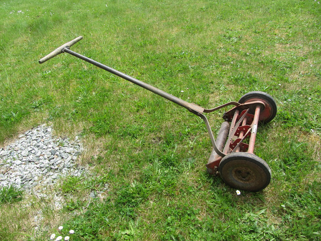 A Craftsman gas push mower parked on pavement beside a lawn