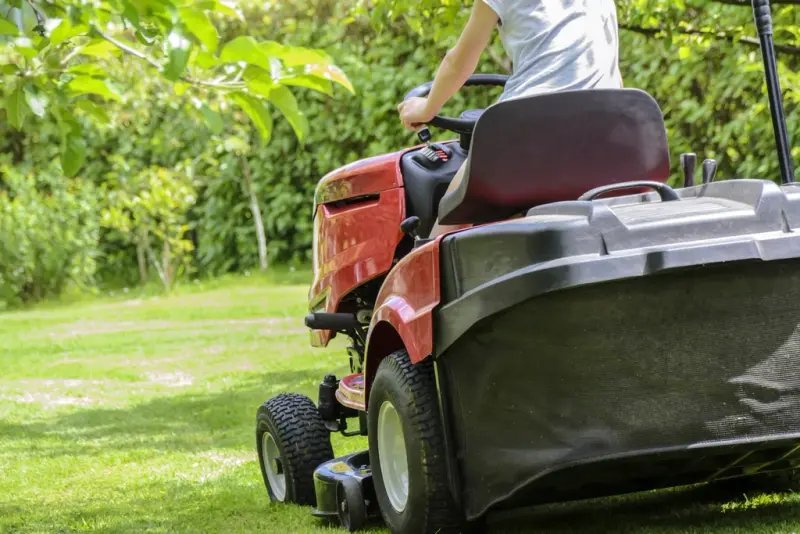A gas push mower standing on a cut green lawn
