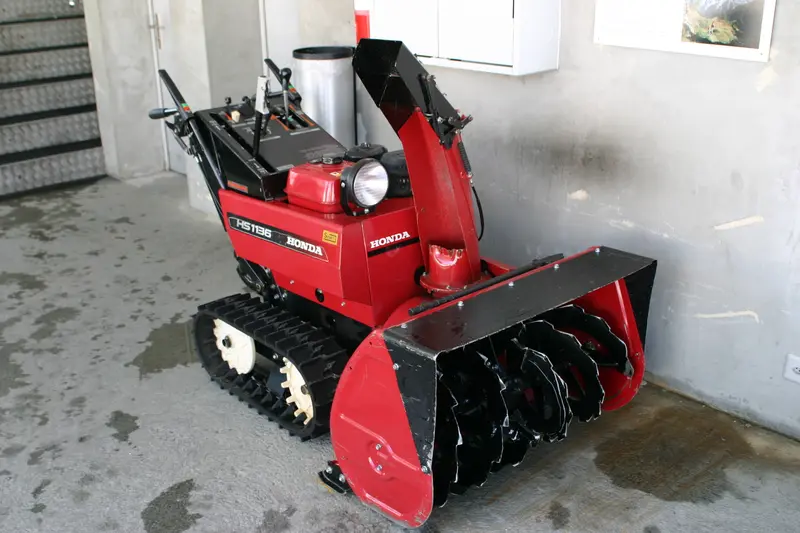 A red Honda HS1136 track-drive two-stage snow blower