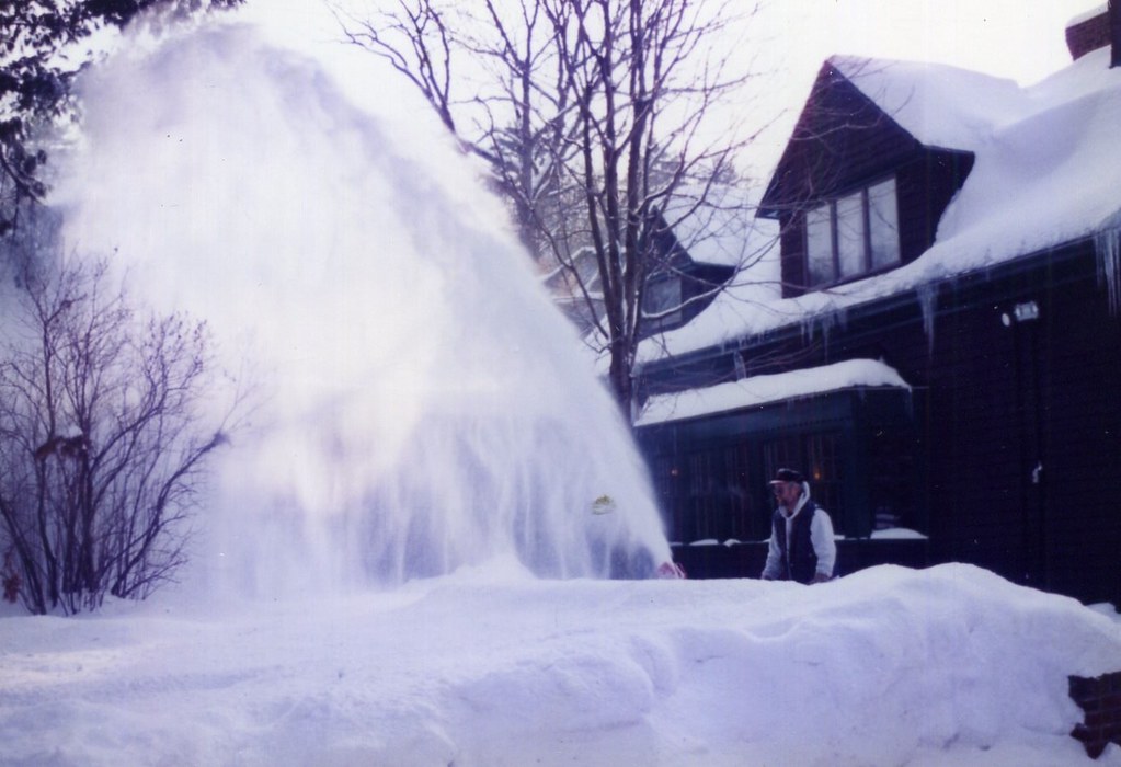A snow blower throwing an arc of snow across a driveway