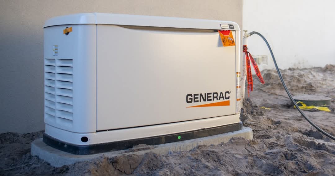 A white Generac standby generator sitting on a fresh concrete pad against a wall, connected to a gas supply line