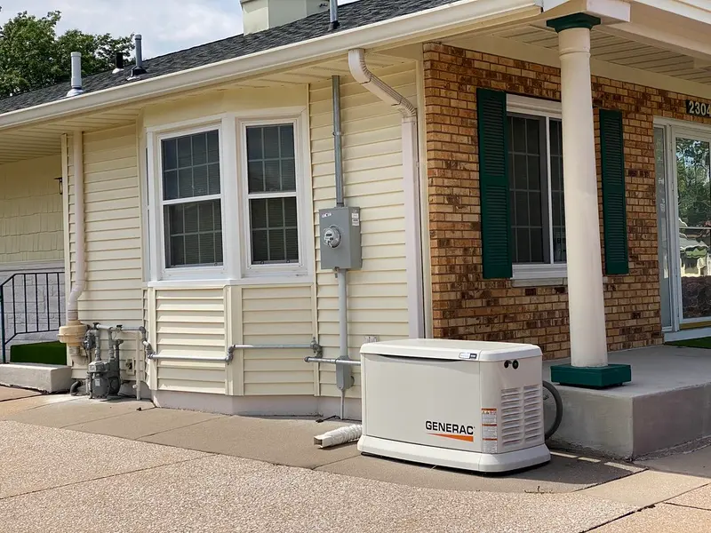 A white Generac standby generator on a driveway beside a house, wired to the gas line and meter