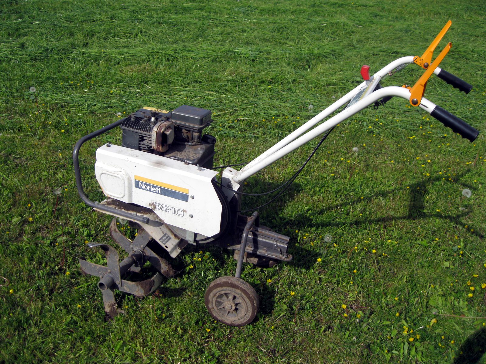 A gas garden tiller with rotating tines parked on soil